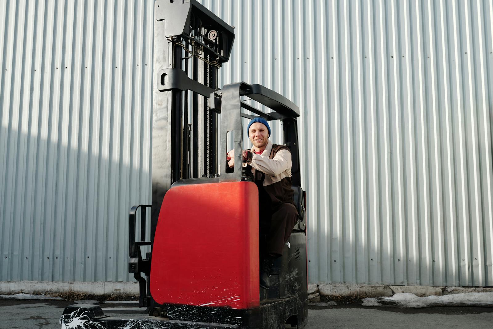 A forklift operator working outdoors in an industrial area with corrugated metal walls.